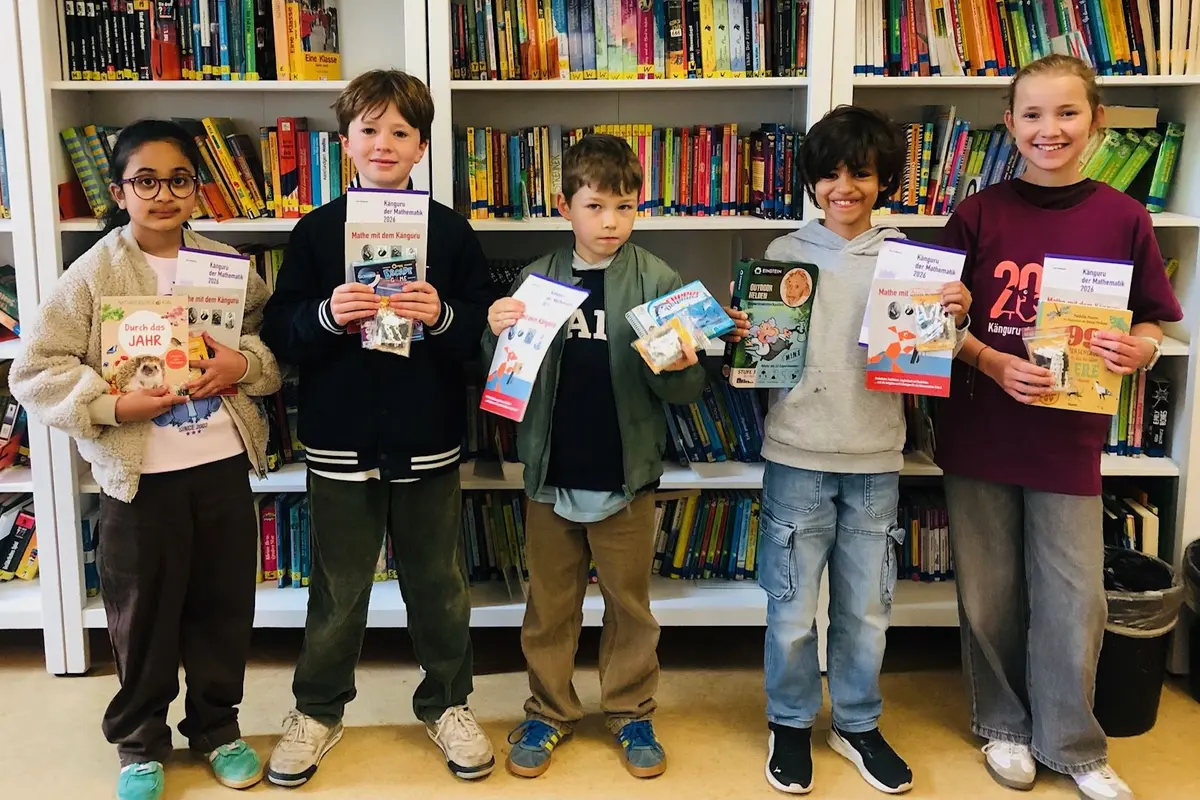 Fünf Kinder stehen vor Bücherregalen und halten Bücher und Zertifikate in die Kamera.