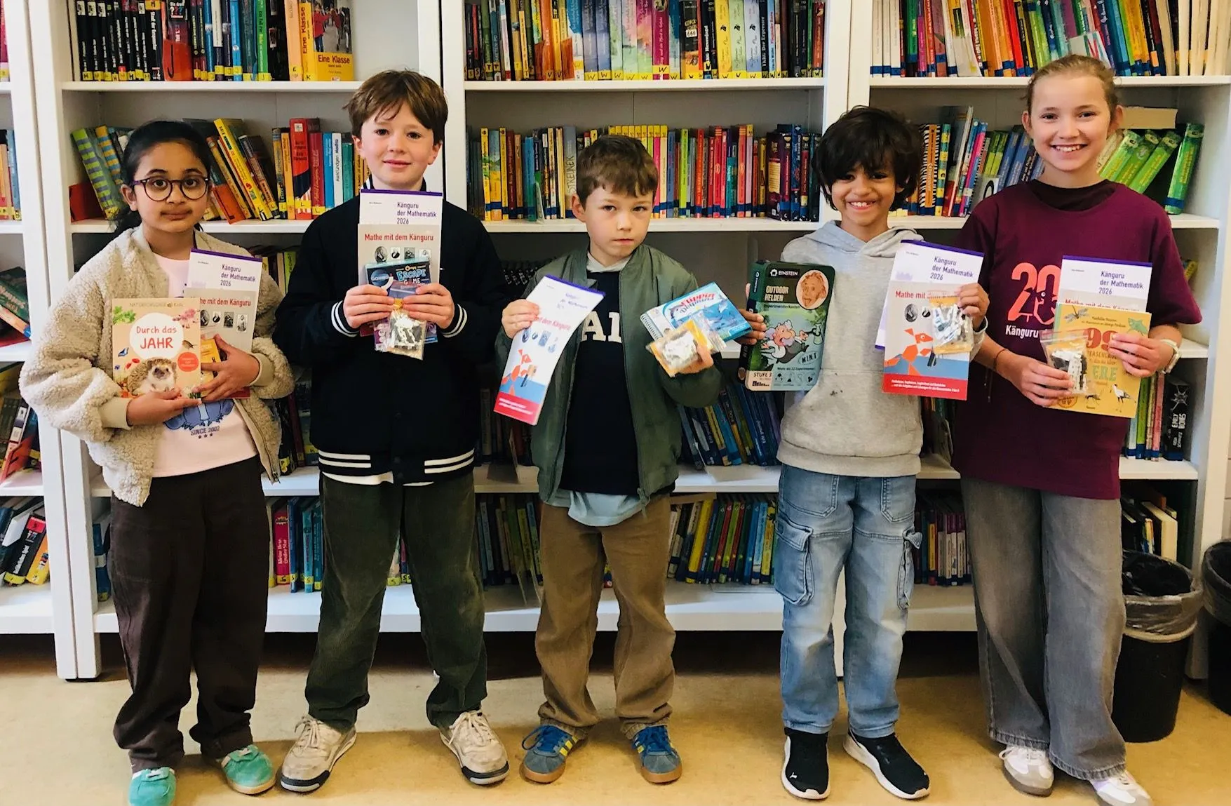 Fünf Kinder stehen vor Bücherregalen und halten Bücher und Zertifikate in die Kamera.
