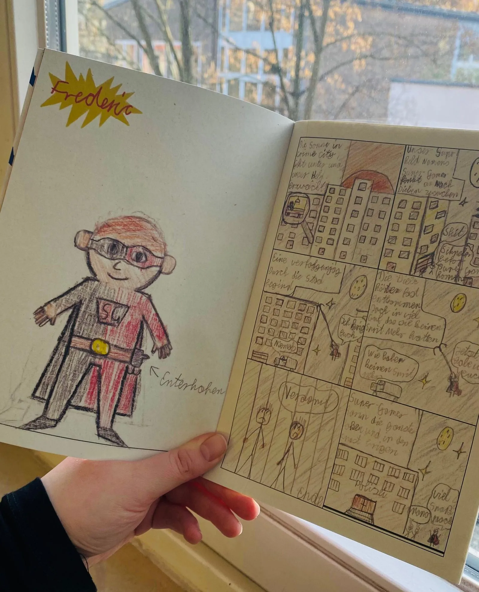 Hand hält Skizzenbuch vor Fenster; links farbiger Superheld, rechts mehrteiliger handgezeichneter Comic mit Gebäuden.