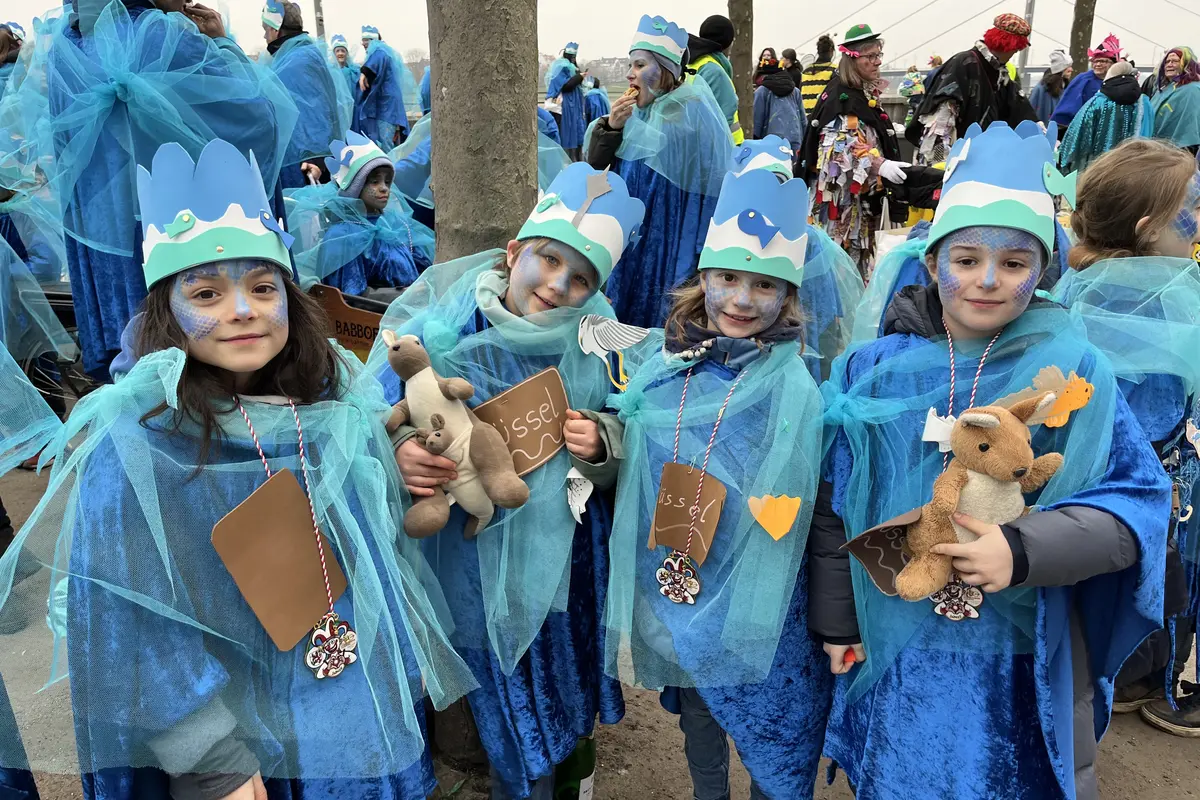 Kinder in blauen Meerjungfrauen‑Kostümen mit Papierkronen, blauem Netzstoff, Gesichtsfarbe und Kuscheltieren