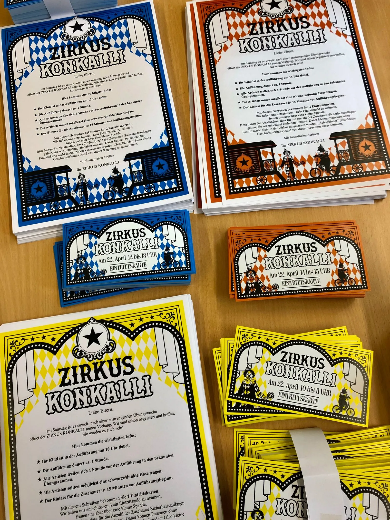 gestapelte bunte Zirkus‑Flyer Zirkus Konkalli in Blau, Orange und Gelb auf Holztisch