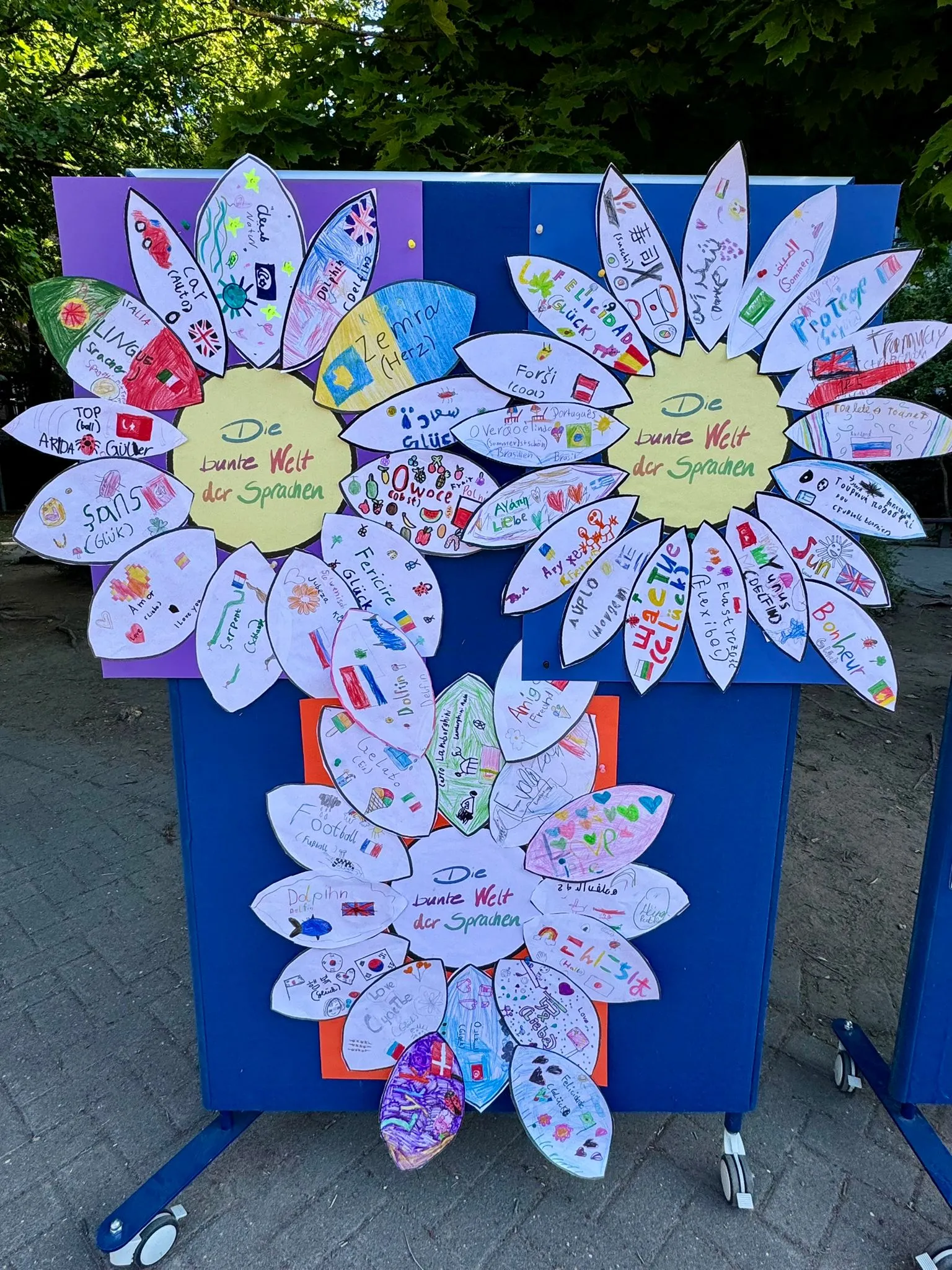 Bunte Papierblätter mit Kinderzeichnungen und Schriftzug Die bunte Welt der Sprachen auf blauem Rollständer