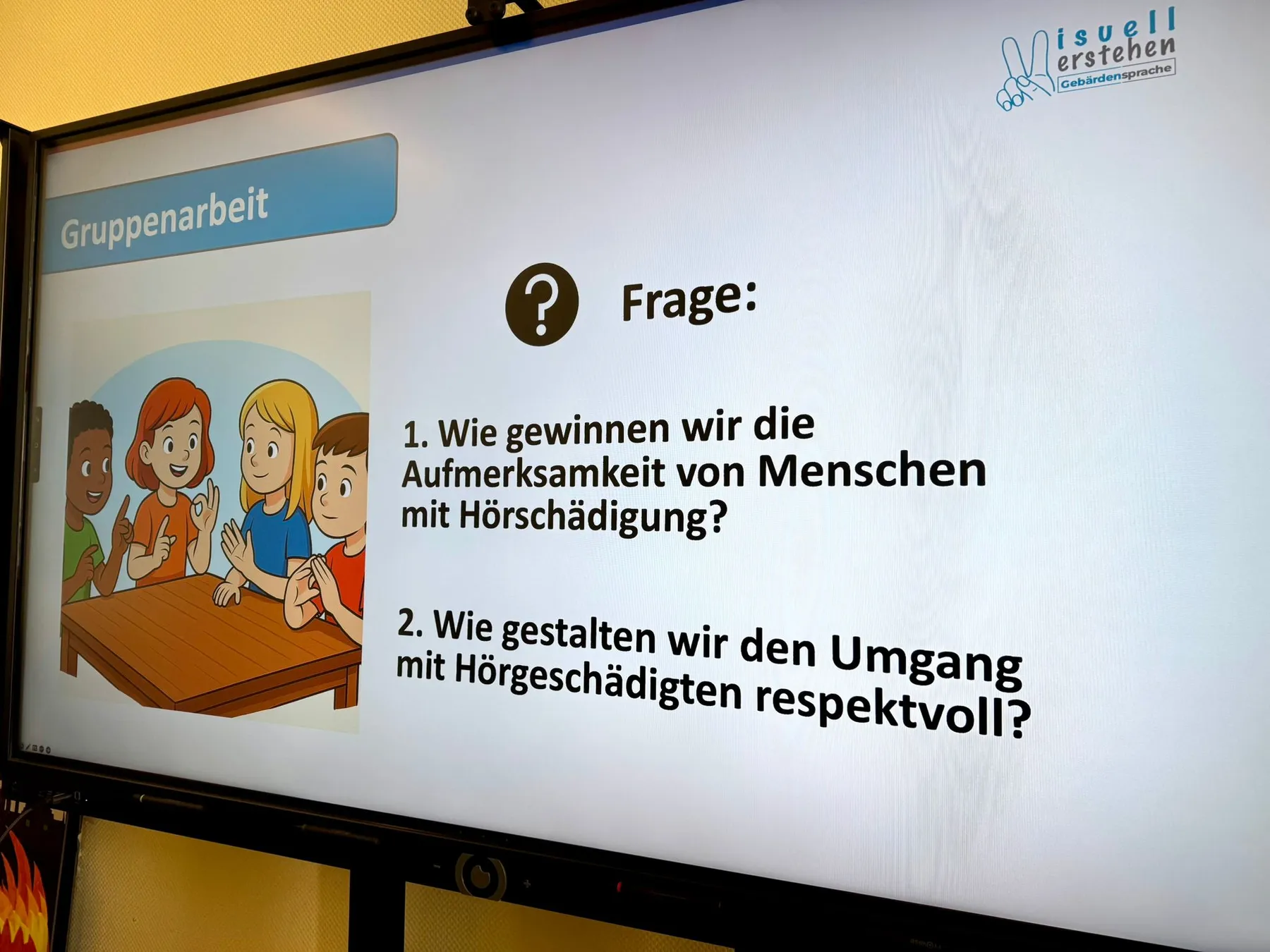 Folienanzeige mit Titel "Gruppenarbeit", Cartoon-Kinder am Tisch und Frage zur Aufmerksamkeit von Menschen mit Hörschädigung