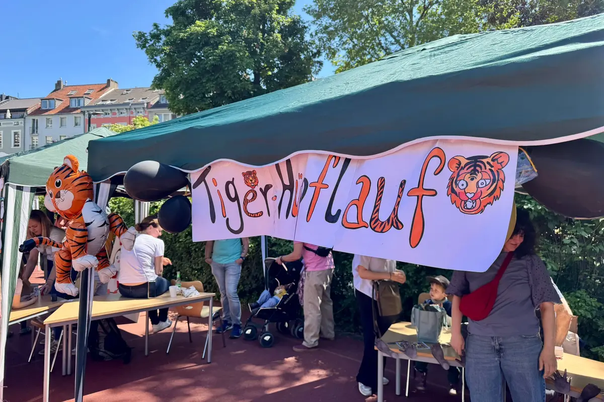 Grüner Pavillion mit Banner „Tigerhilfe“, Tiger-Luftballons und mehreren Personen darunter