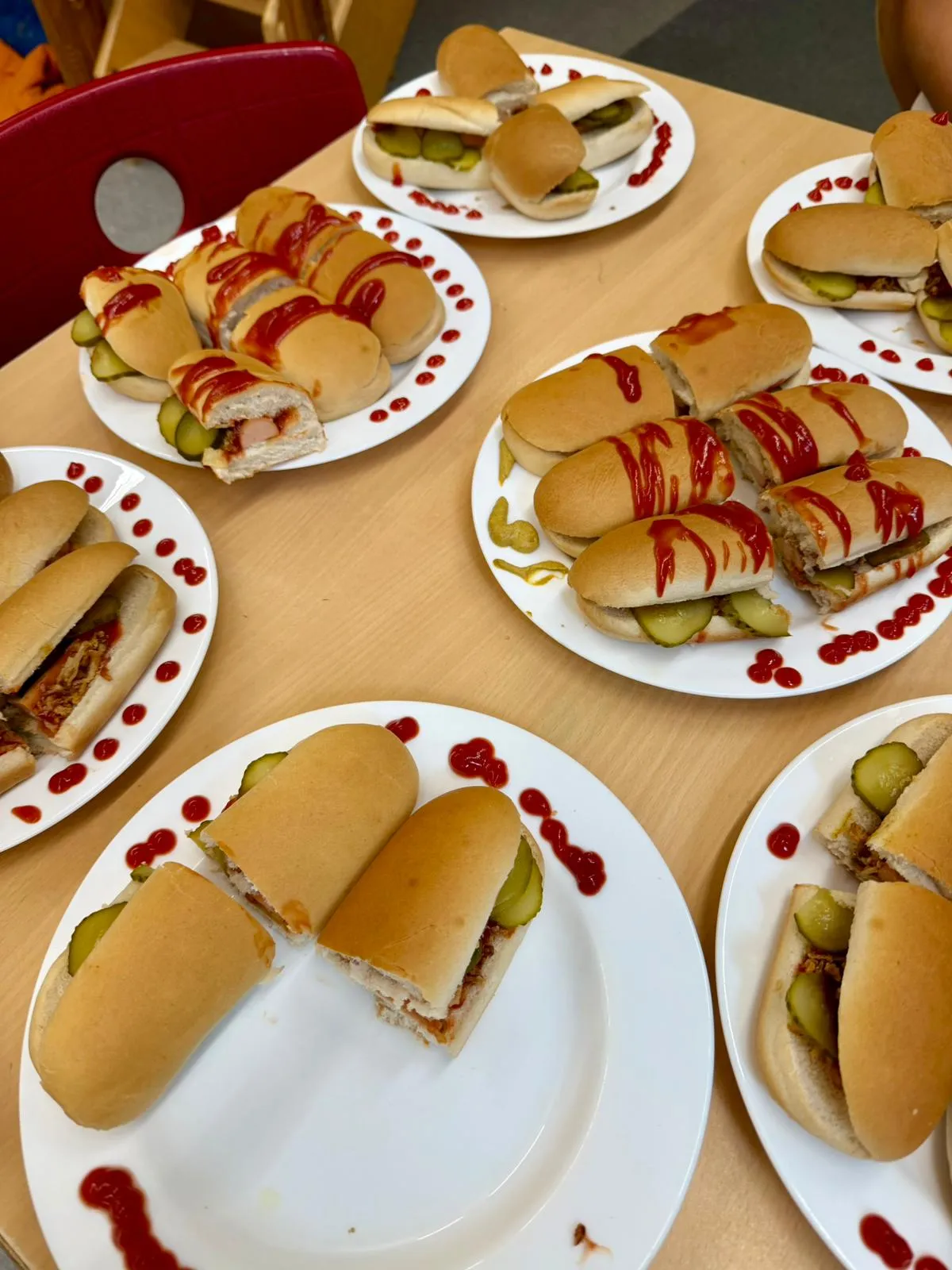 Teller mit vielen aufgeschnittenen Würstchenbrötchen, Gewürzgurken und Ketchup auf Holztisch