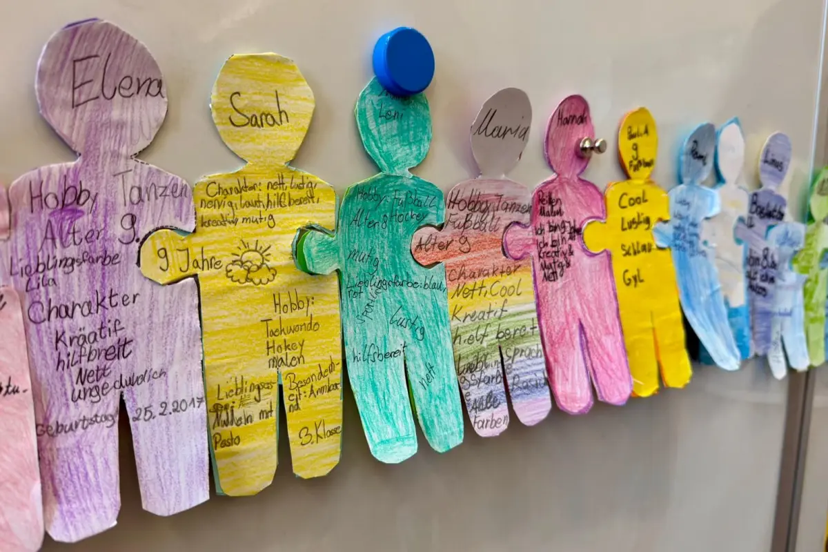 Bunte, handbeschriebene Pappfiguren an einem Whiteboard, mit Magneten und Pinnnadeln befestigt