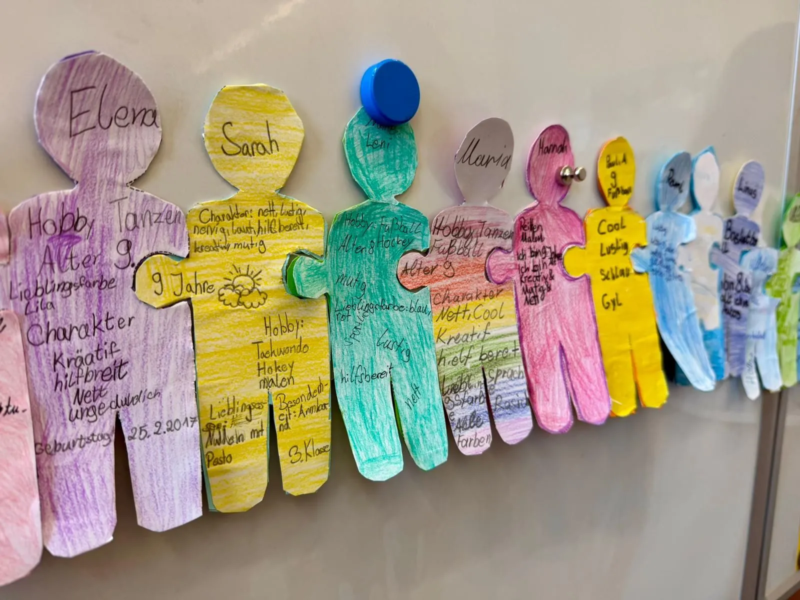 Bunte, handbeschriebene Pappfiguren an einem Whiteboard, mit Magneten und Pinnnadeln befestigt