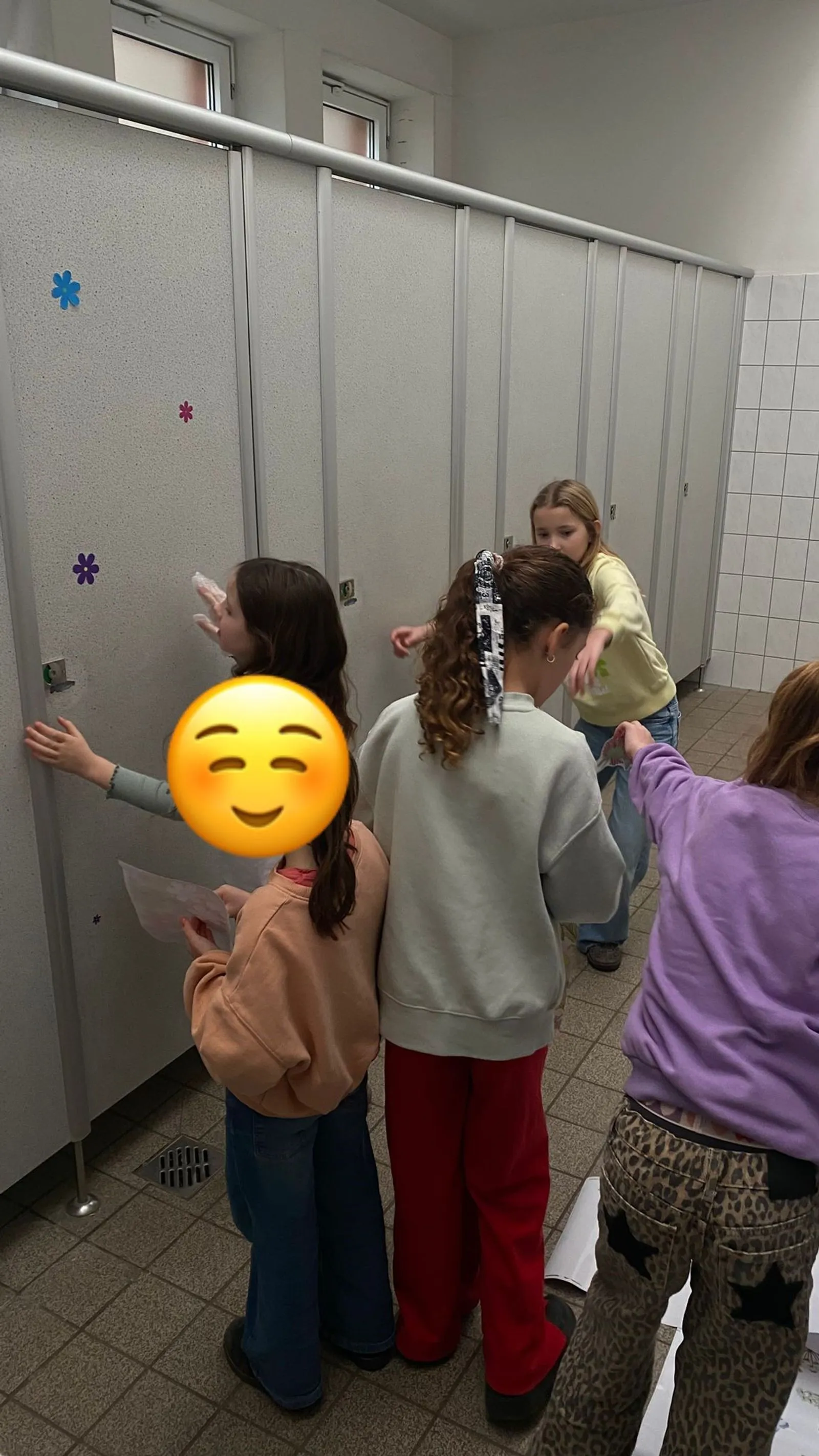 Mehrere Mädchen in einer Sanitärzone kleben bunte Blumenaufkleber an Toilettenkabinen