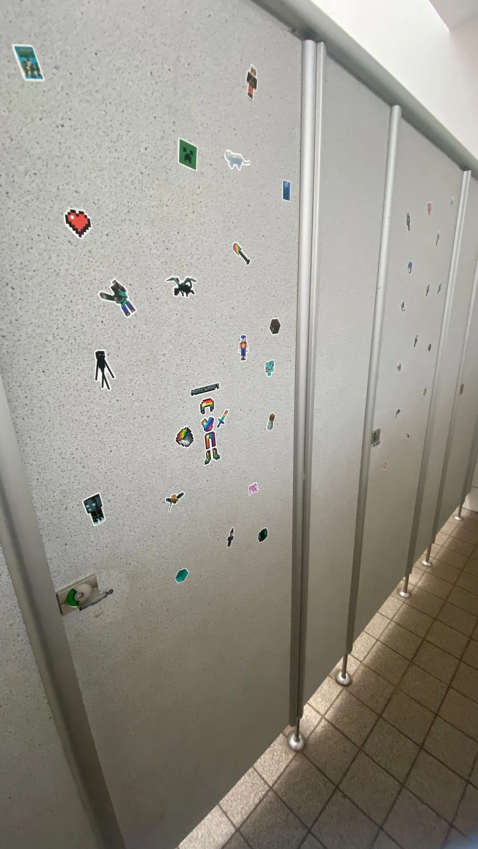 Graue Toilettenabtrennungen mit bunten, pixeligen Stickern auf den Türen und gefliestem Boden