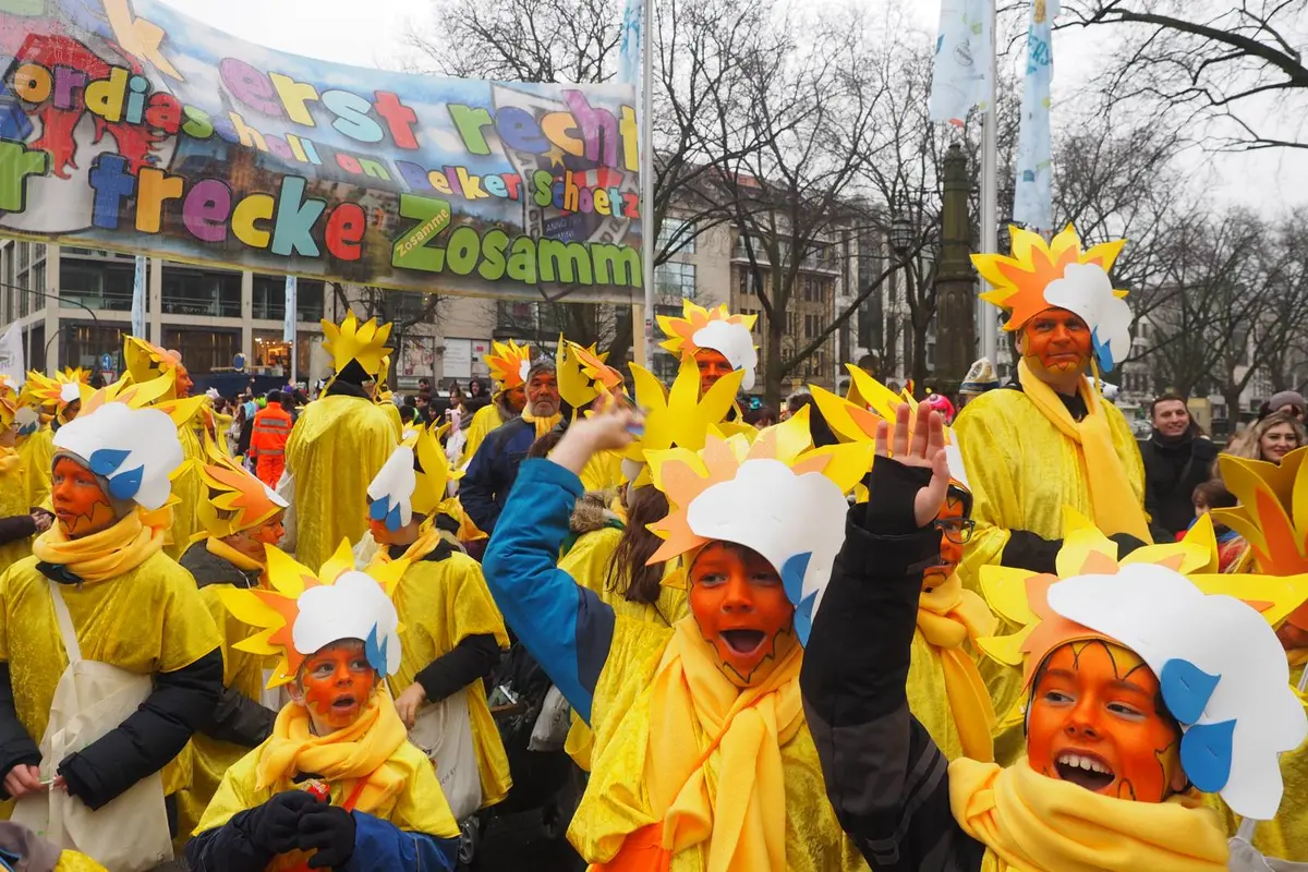 Gruppe verkleideter Kinder und Erwachsener in gelben Sonnenkostümen mit orangen Gesichtern und Papiersonnenkopfschmuck