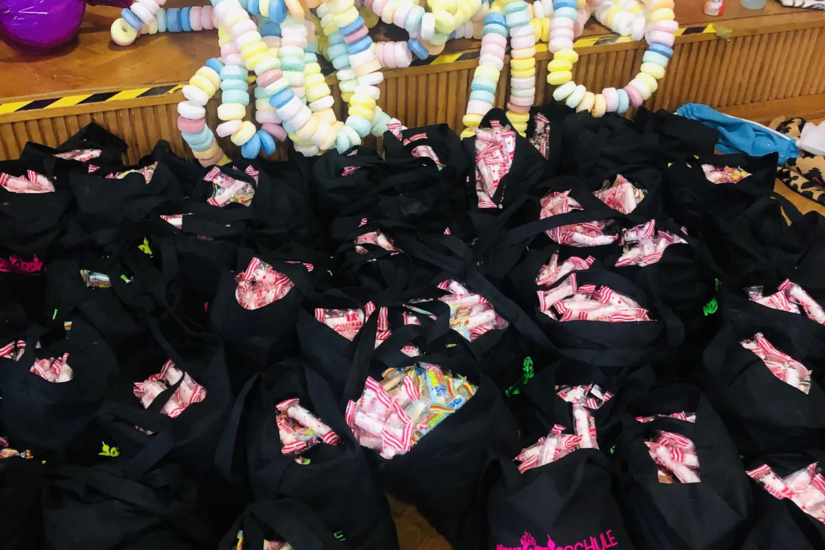 Viele schwarze Taschen voller Süßigkeiten vor einer Bühne, darauf große bunte Pastell-Süßigkeitenketten