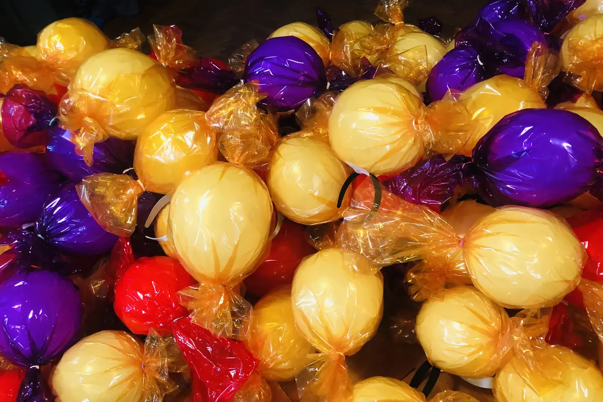 Viele gelbe, violette und rote Luftballons in glänzender, transparenter Verpackungsfolie arrangiert