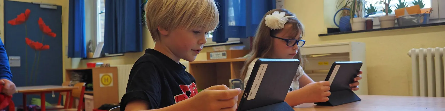 Zwei Kinder sitzen an einem Tisch und benutzen Tablets in einem Klassenraum.