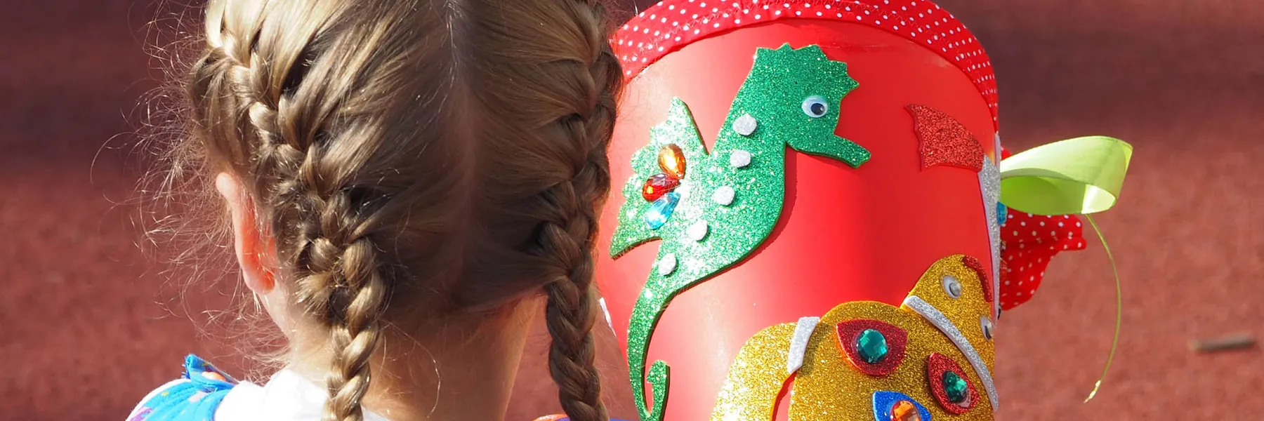 Kind von hinten mit zwei geflochtenen Zöpfen und roter Schultüte mit glitzerndem Seepferdchen