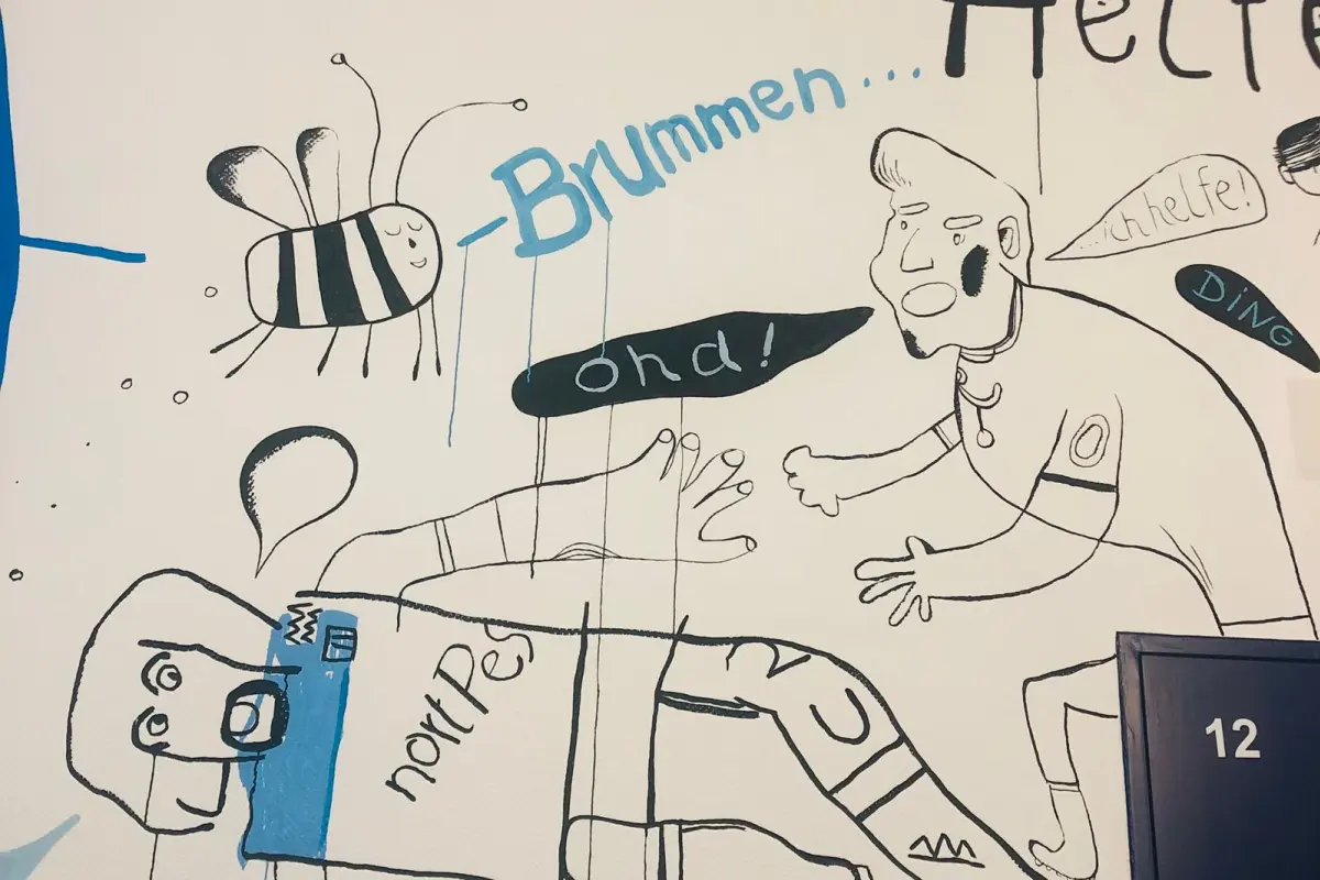 Wandzeichnung mit zwei cartoonhaften Figuren, einer Biene, Sprechblasen mit „Brummen...“, Türschild „Klasse“ und Zahl 12