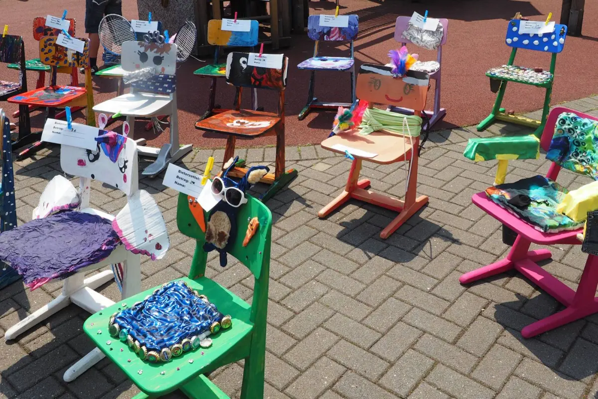 Bunte, individuell dekorierte Kinderstühle auf gepflastertem Platz mit Federn, Stoffen und verschiedenen Verzierungen