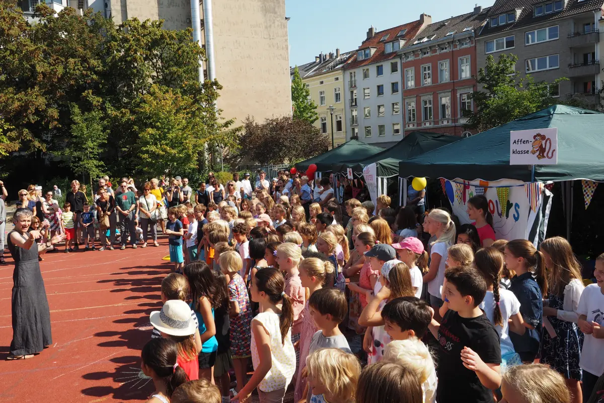 Große Gruppe Kinder und Erwachsene auf sonnigem Schulhof/Sportplatz bei Fest mit Zelten und bunten Dekorationen