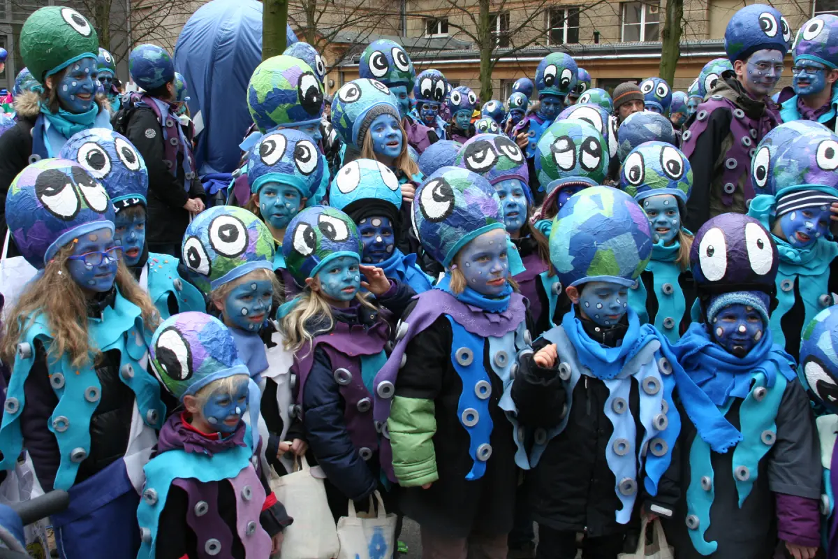 Gruppe verkleideter Menschen mit blau bemalten Gesichtern und bunten, kugeligen Hüten mit großen Augenmotiven